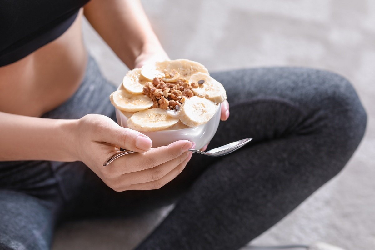 Sporty woman eating tasty yogurt at home, closeup